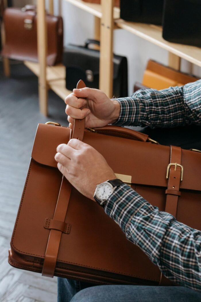 A close-up shot of a man's hands adjusting a brown leather briefcase indoors.
