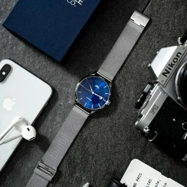 Stylish flat lay showcasing technology devices, watch, and accessories on dark surface.