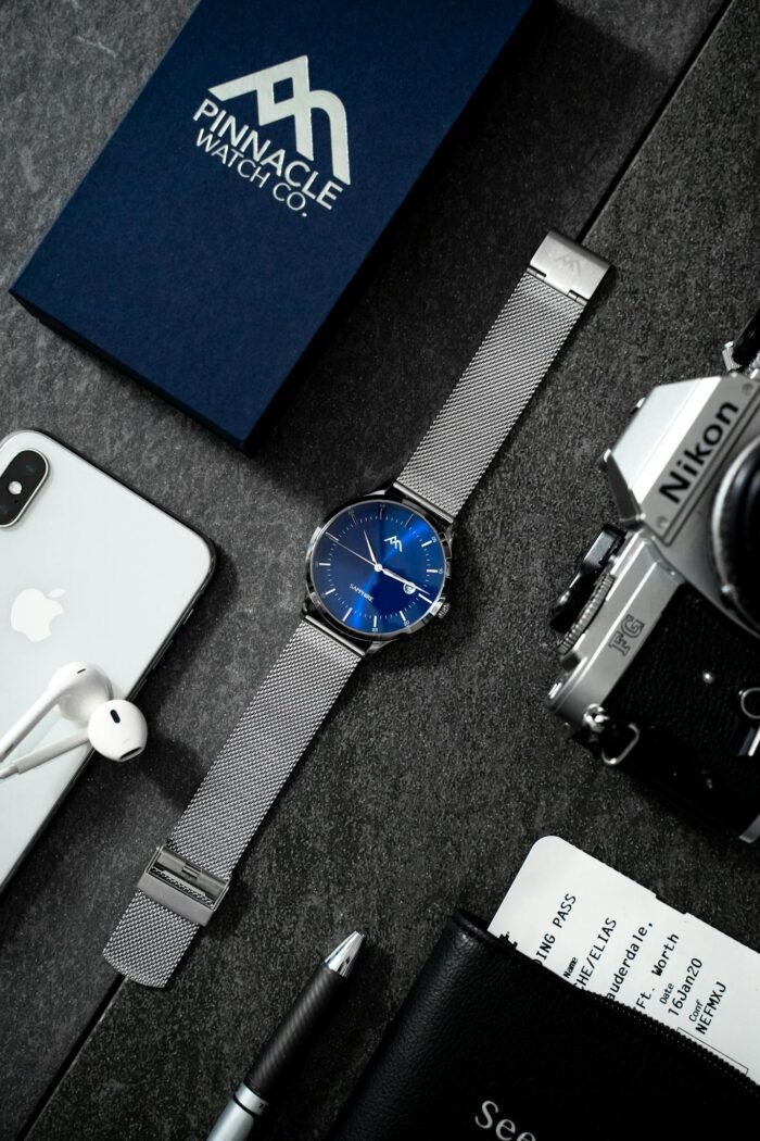 Stylish flat lay showcasing technology devices, watch, and accessories on dark surface.